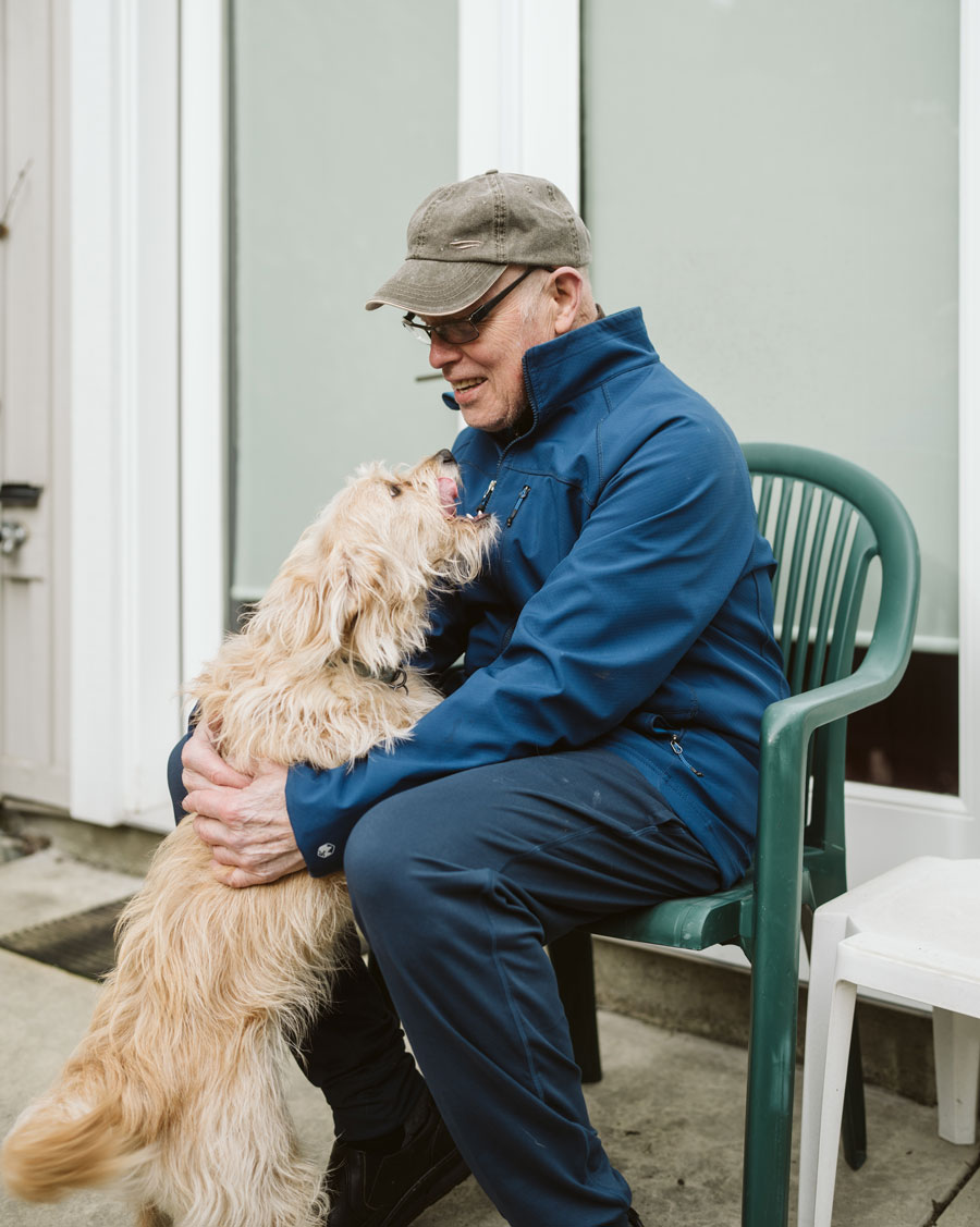 A senior man petting his dog while sitting on a chair