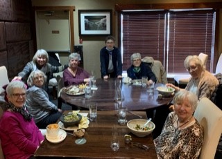 A support group of ladies sits together around a table, with food.